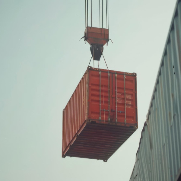 Grue soulevant un container maritime rouge illustrant sa structure et son usage dans le transport