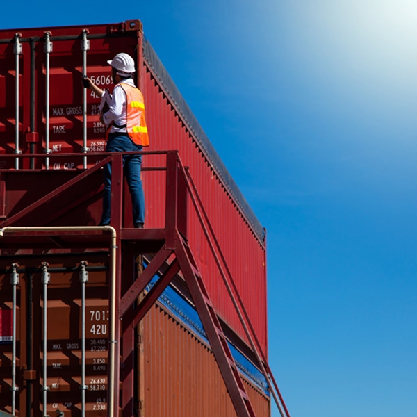 Technicien en casque et gilet grimpant sur un conteneur rouge lors d'une livraison à Montréal