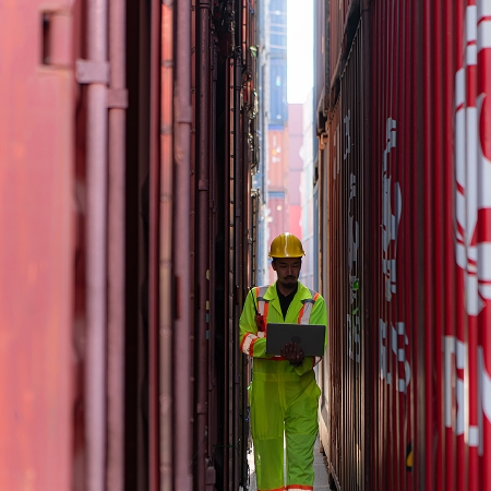 Technicien en équipement de sécurité naviguant entre des rangées de conteneurs usagés dans un parc de transport