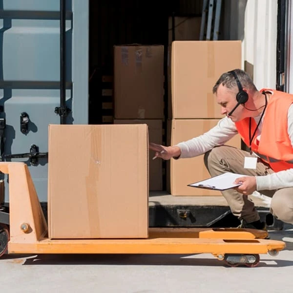 Un homme en gilet orange se tient à côté d'une palette.